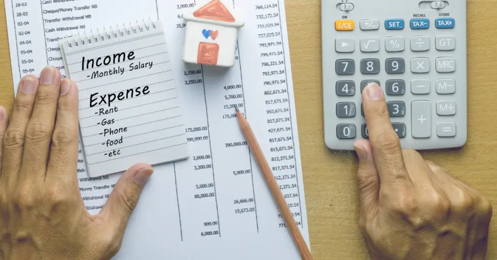 Image of two hands on a desk with a list of income and expenses and a calculator.
